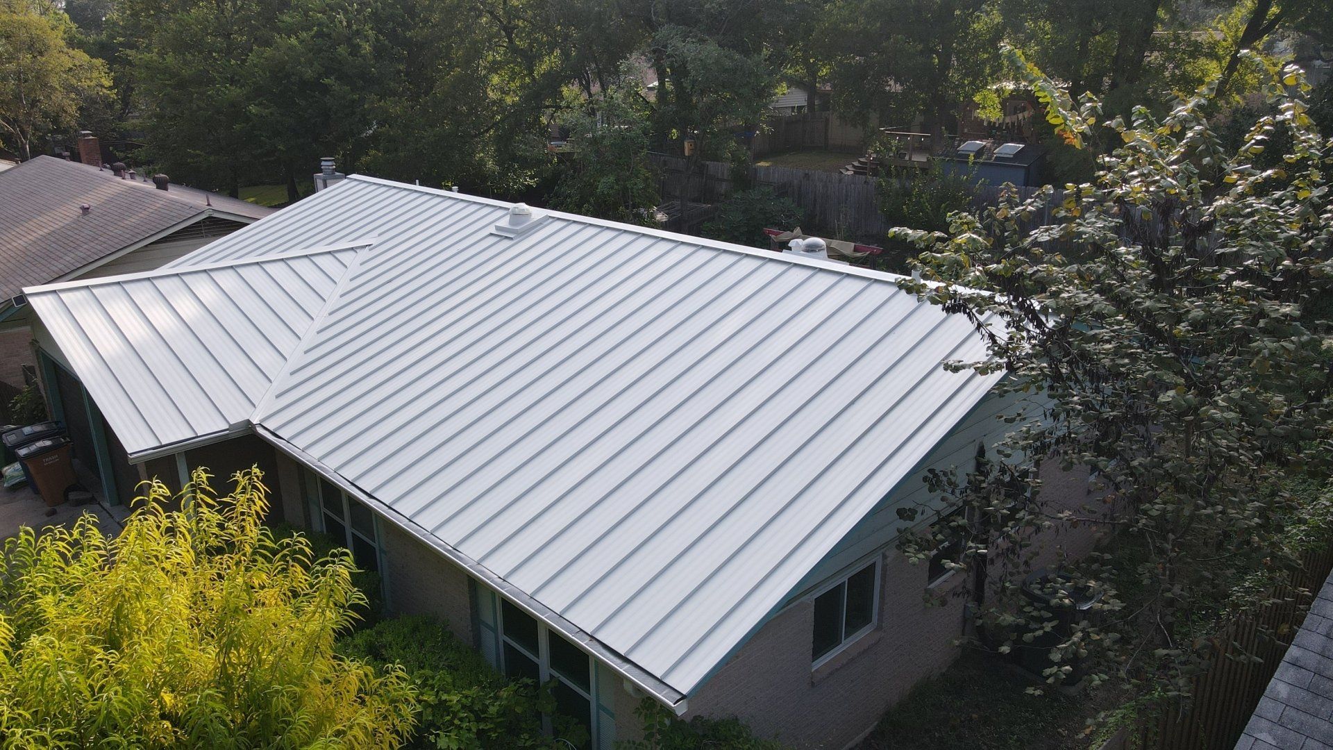 An aerial view of a house with a metal roof surrounded by trees.