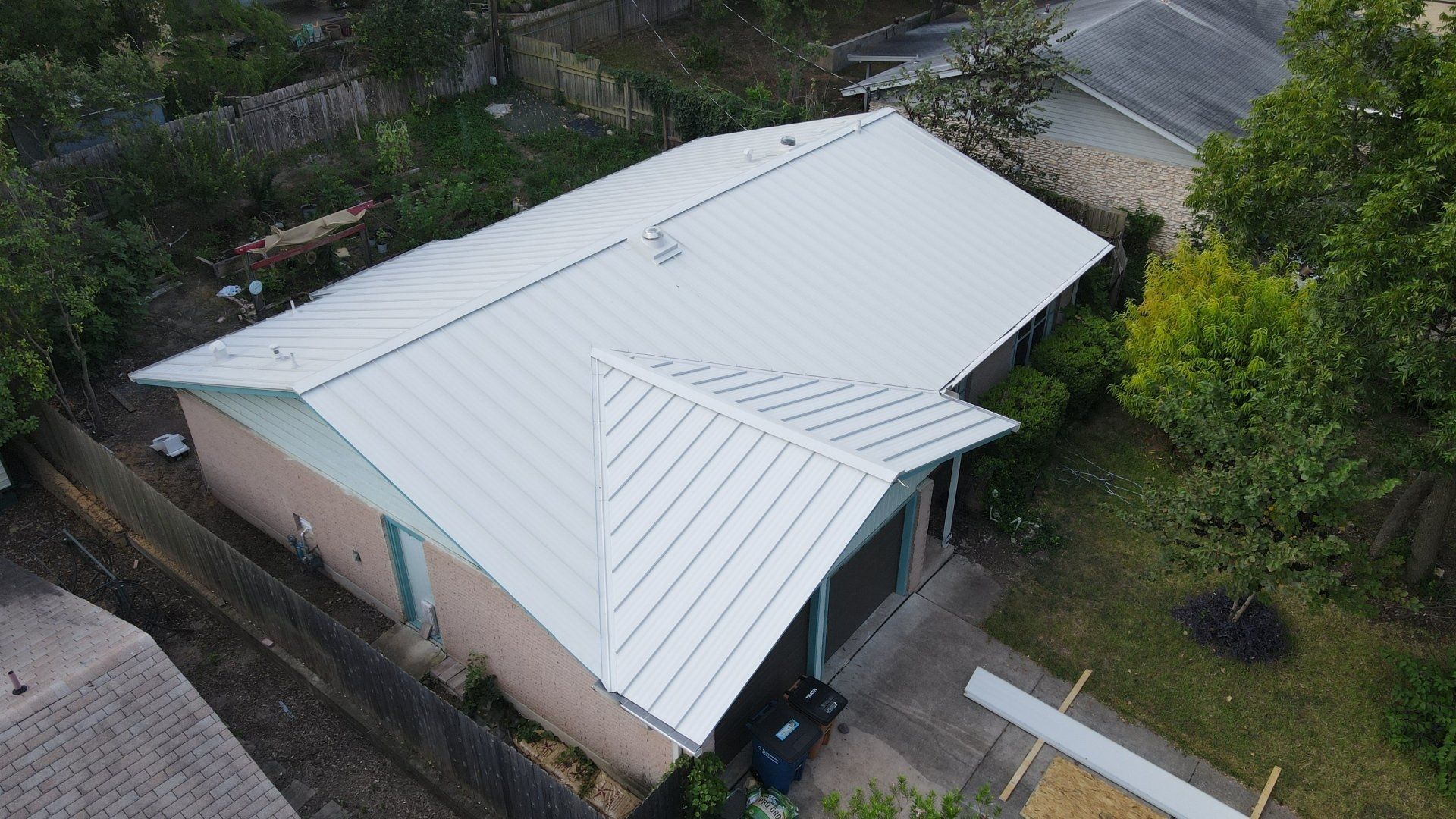 Aerial view of a white-roofed house beside trees and a driveway