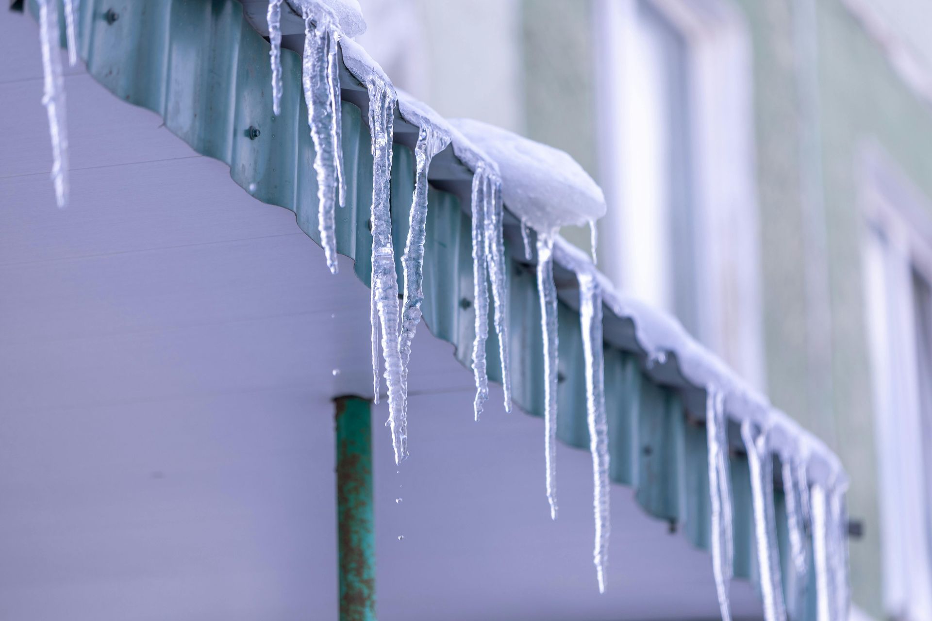 Icicles hanging from a green-roofed overhang in winter.