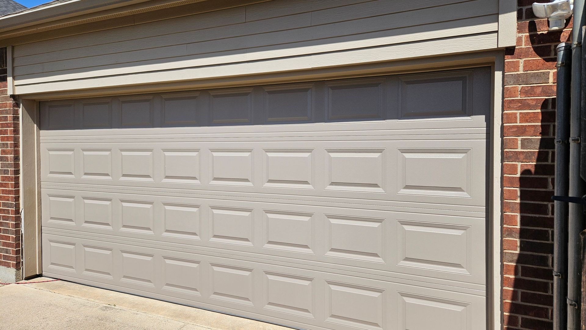 Tan garage door with square panel design; brick exterior.