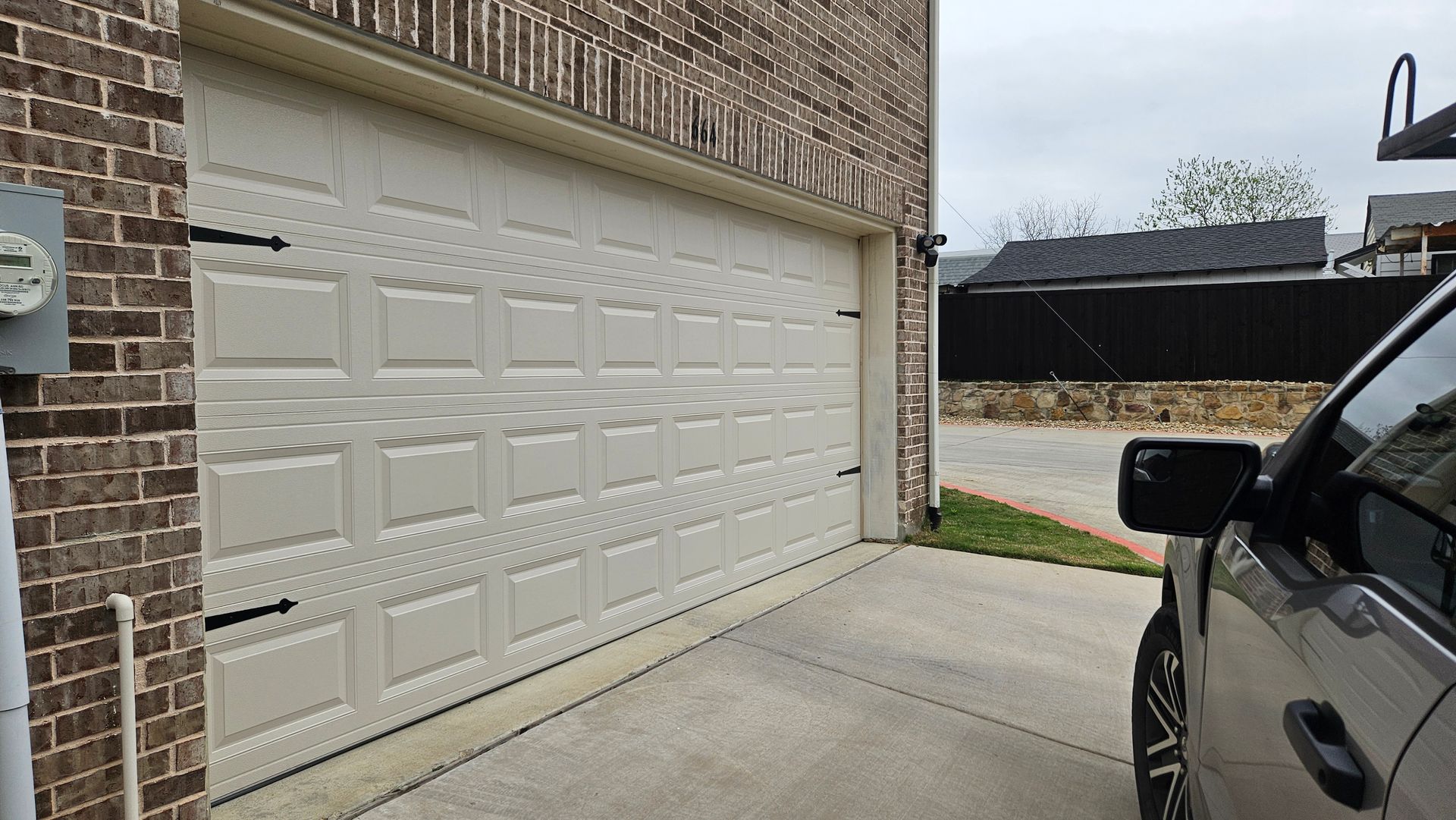 Garage door with a vehicle parked in front, located beside a brick wall.