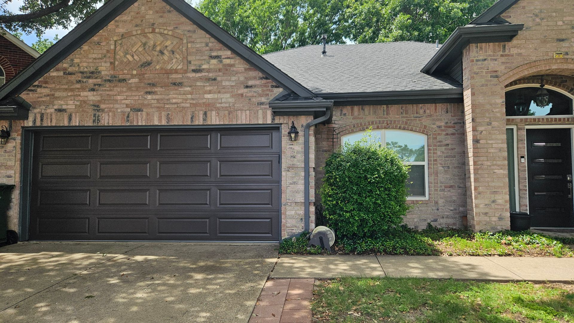 Brown brick house with dark garage door, arched window, and front door.