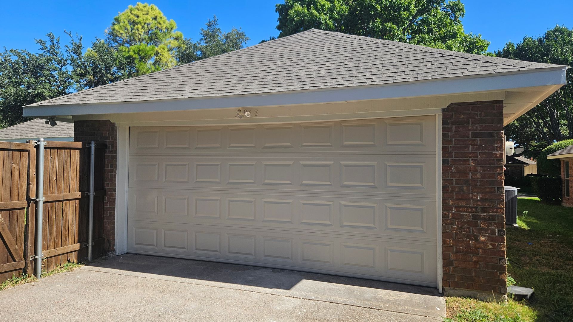 Tan garage with gray roof, brick sides, and closed garage door in a suburban setting.