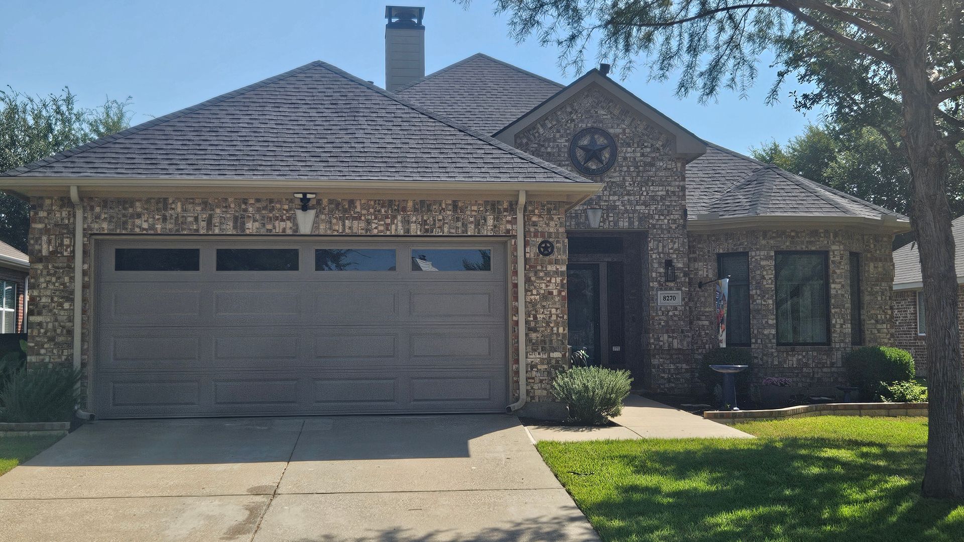 Tan brick house with gray garage door, brown roof, and small lawn.