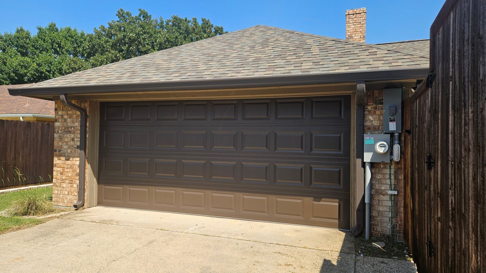Brown garage with stone facade and roof, next to a wooden fence.