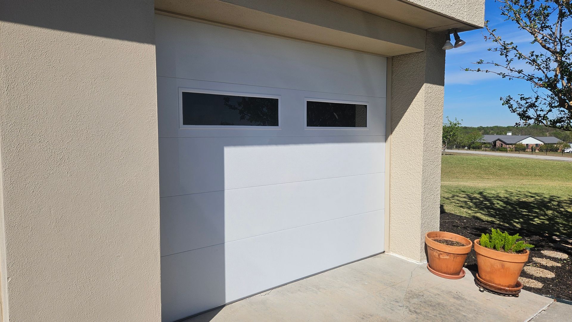 White garage door with windows, stucco exterior, and potted plants on a concrete surface.