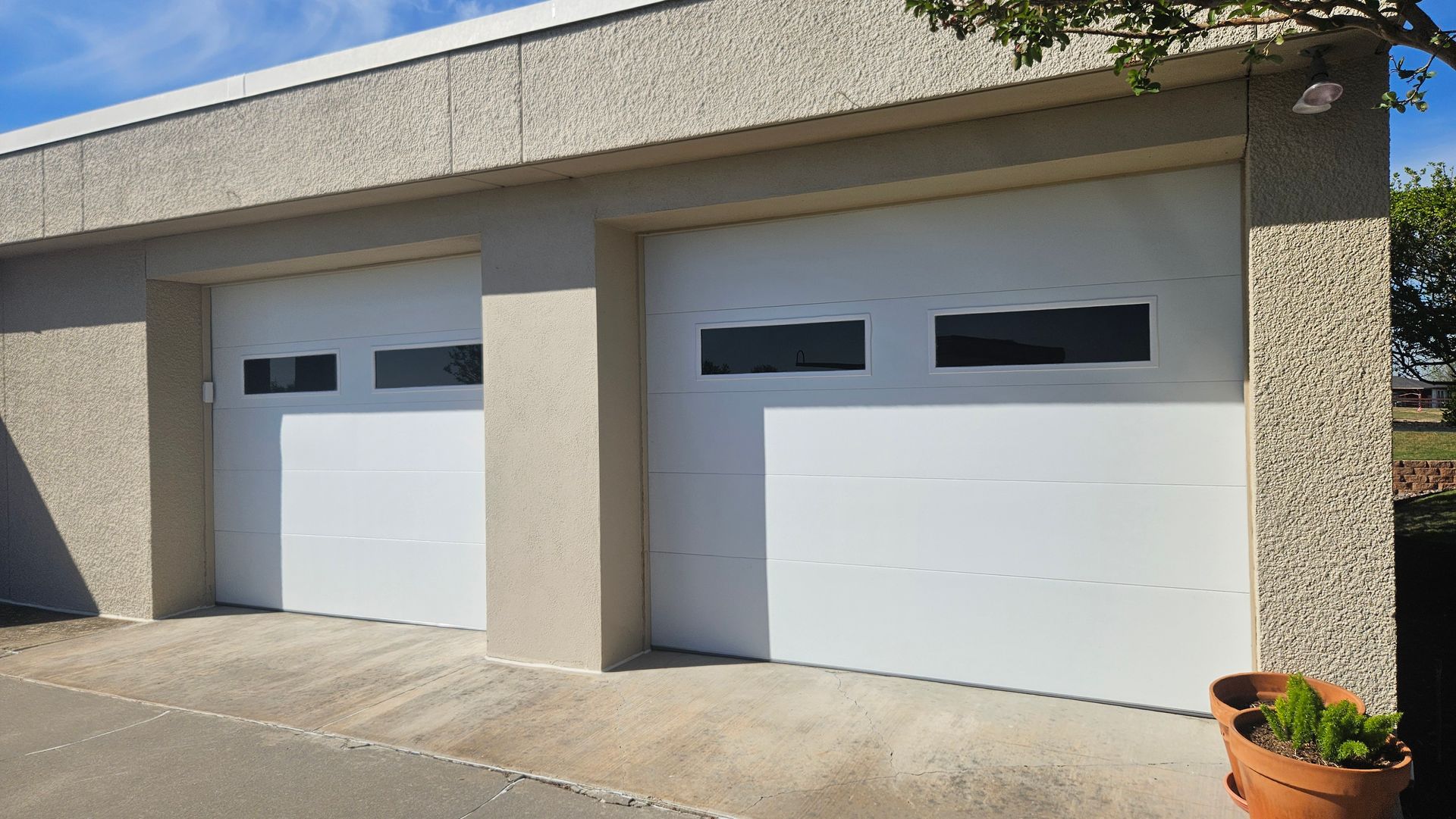 Two white garage doors with rectangular windows, on a concrete building.