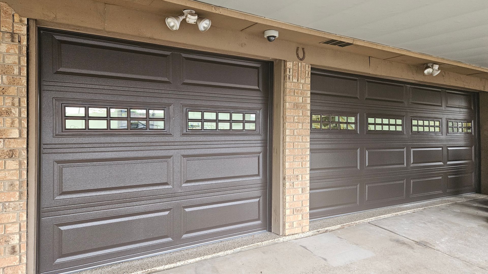 Brown garage doors with windows, flanked by brick, under a light-colored roof.