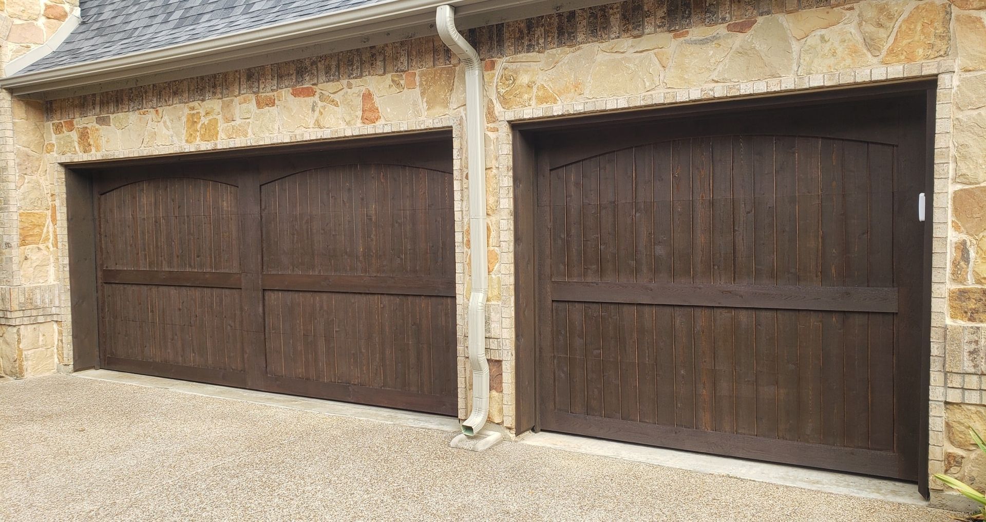 A pair of wooden garage doors on a brick building.