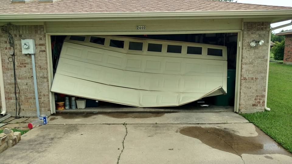 A garage door has fallen off of a brick house.