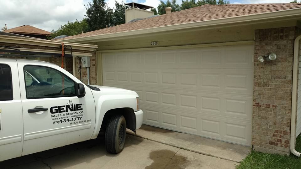 A white genie truck is parked in front of a garage door