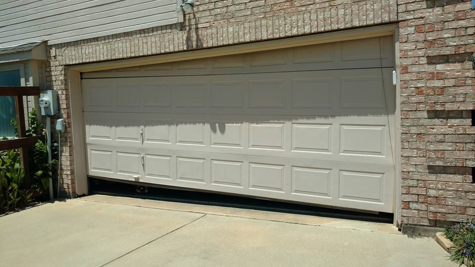 A white garage door is open in front of a brick house.