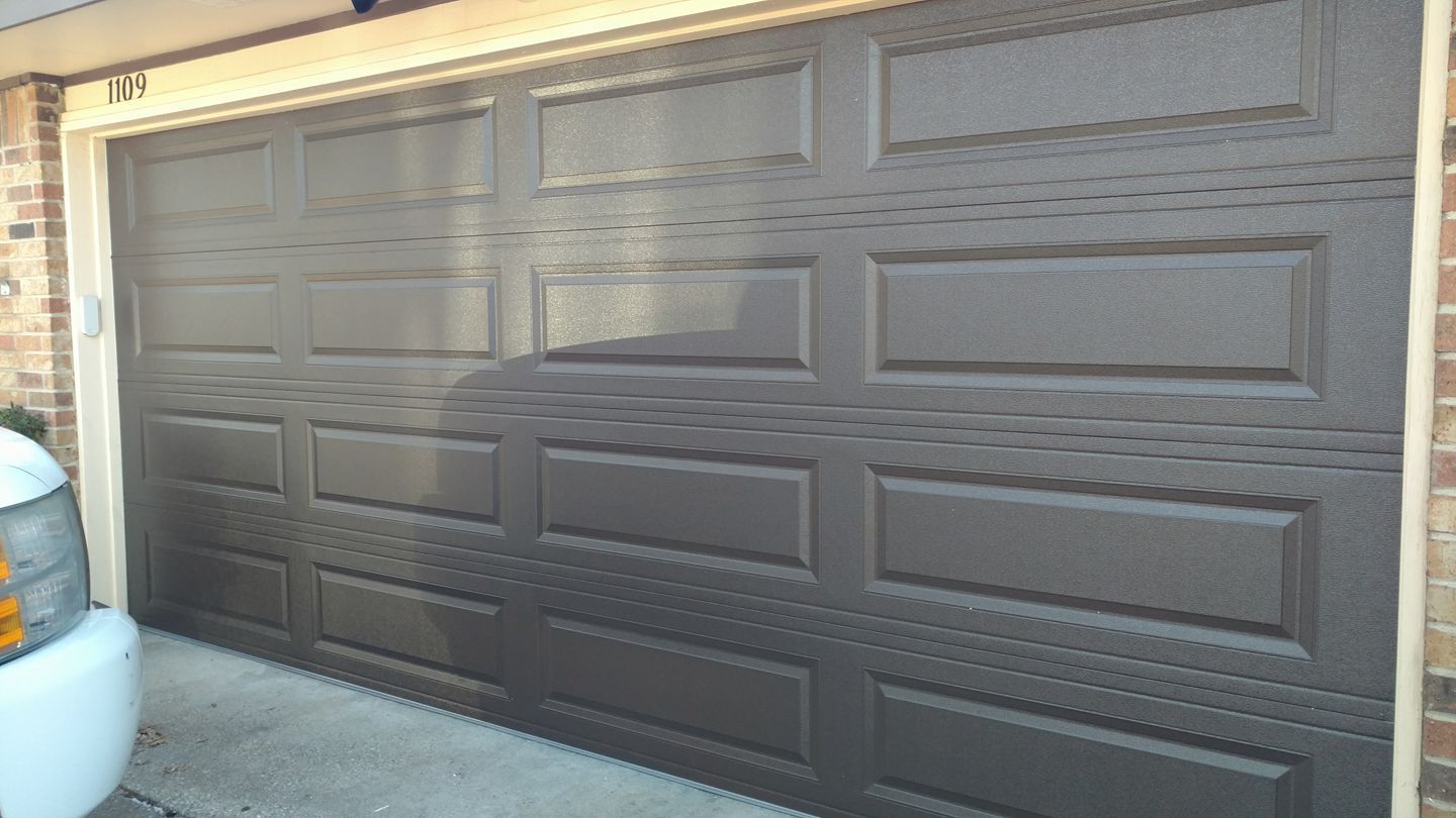 A brown garage door is sitting in front of a brick house.