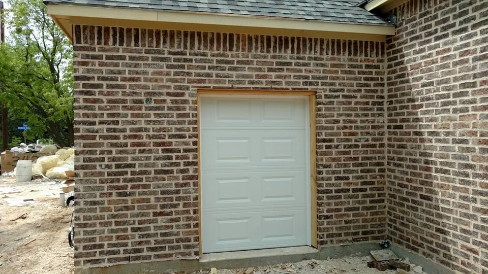 A white garage door is on the side of a brick building.