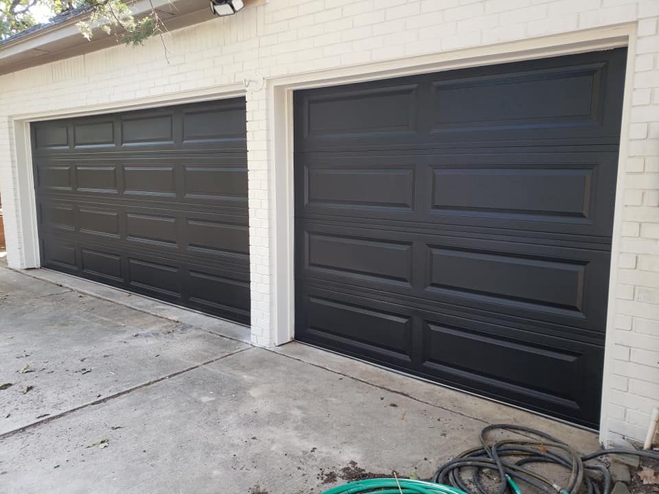 A couple of black garage doors on a white brick building.