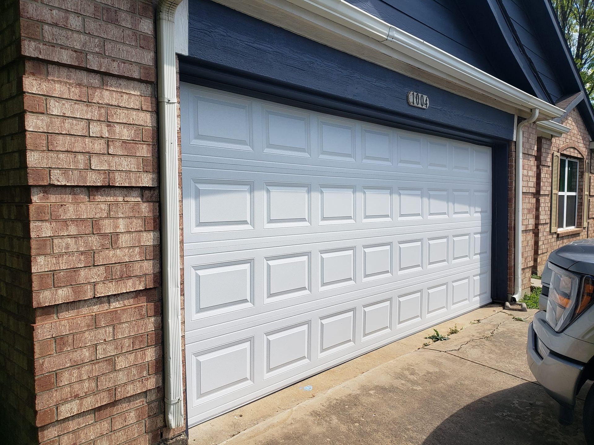 A white garage door is sitting in front of a brick house.
