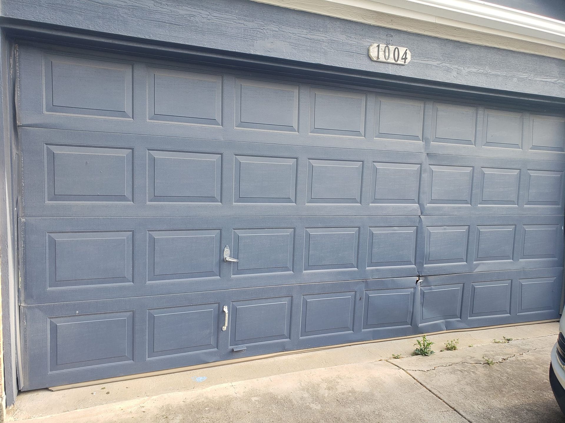 A blue garage door with a car parked in front of it.