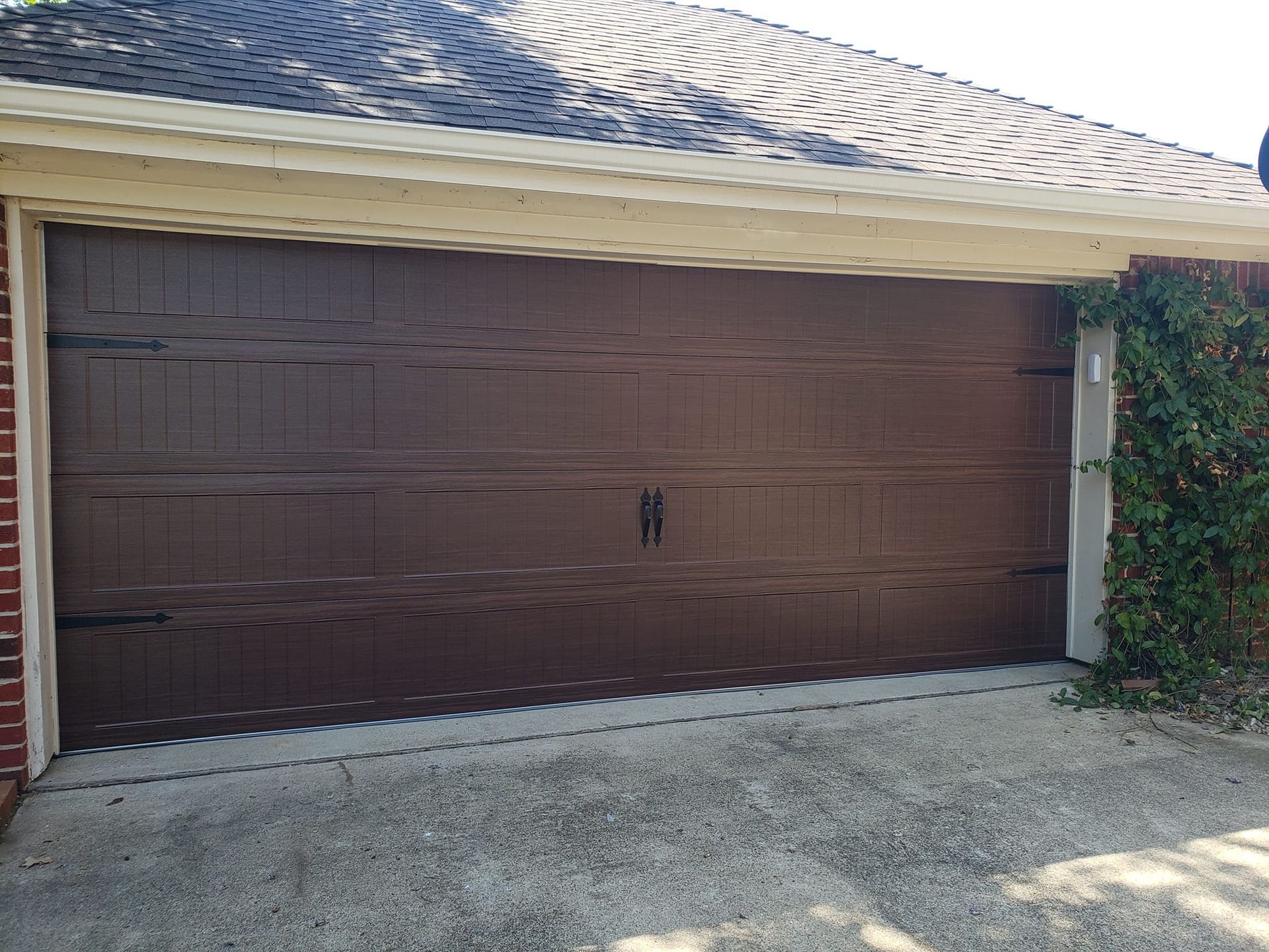 A brown garage door is sitting in front of a brick house.