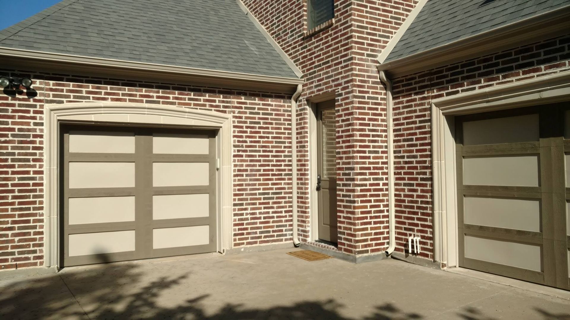 There are two garage doors on the side of a brick house.