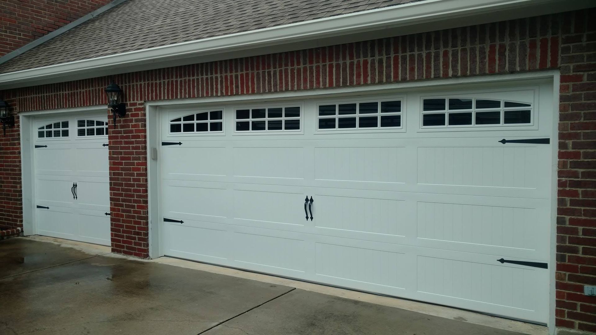 Three white garage doors are on a brick building.