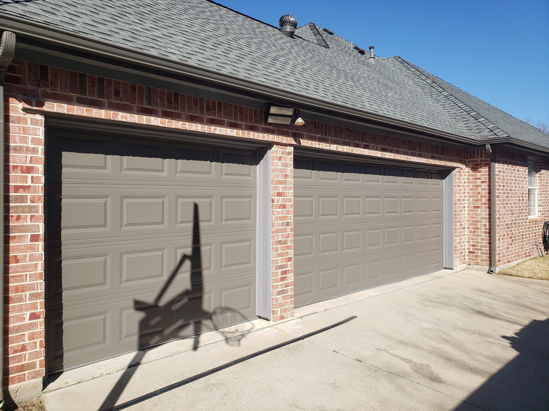 There are two garage doors on the side of a brick house.