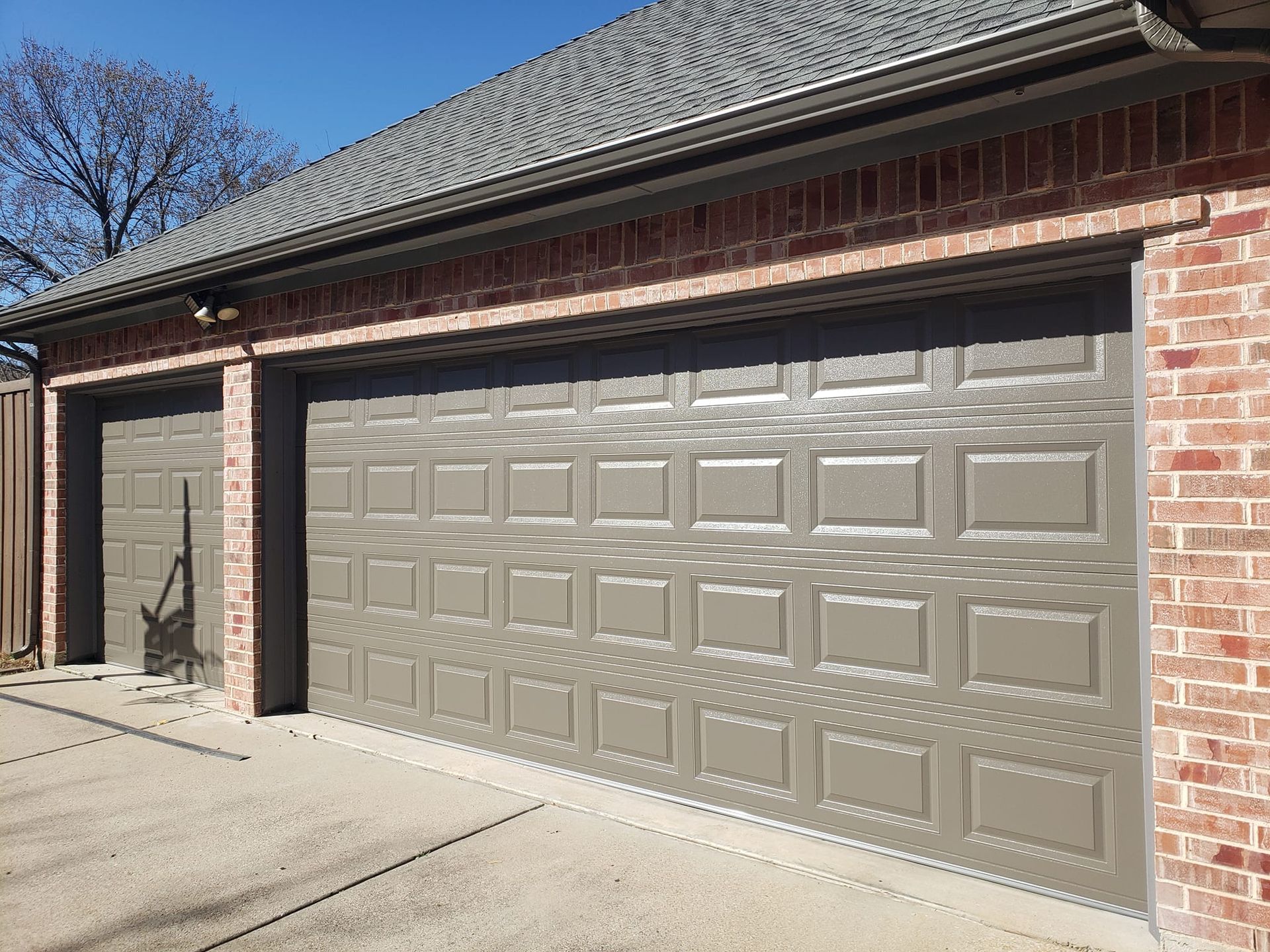 There are two garage doors on the side of a brick house.