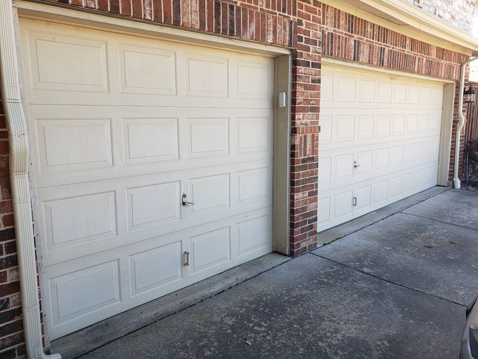 Two white garage doors are sitting next to each other on a brick building.