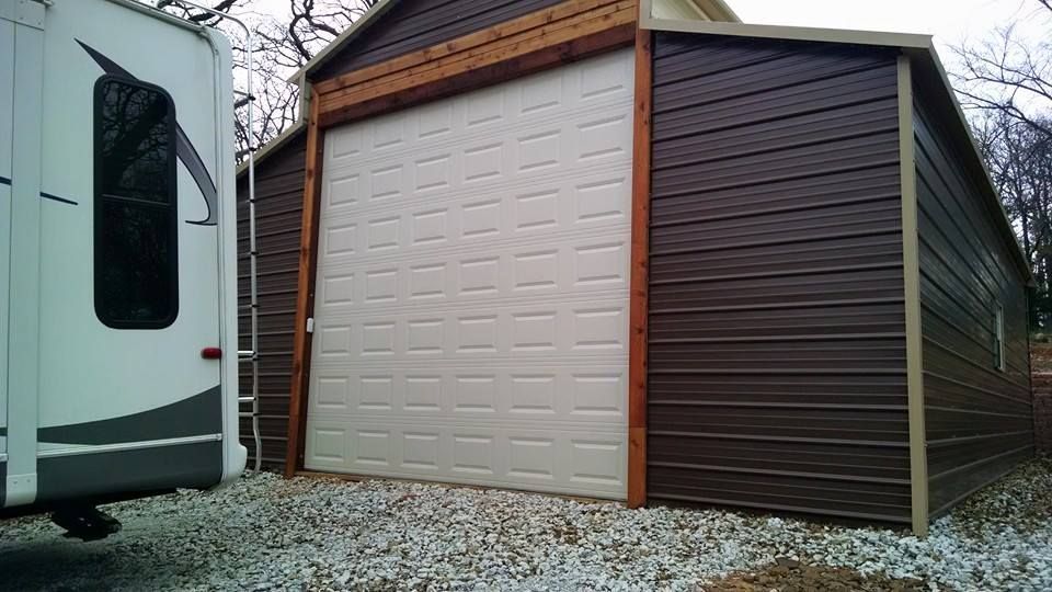 A white trailer is parked next to a brown garage