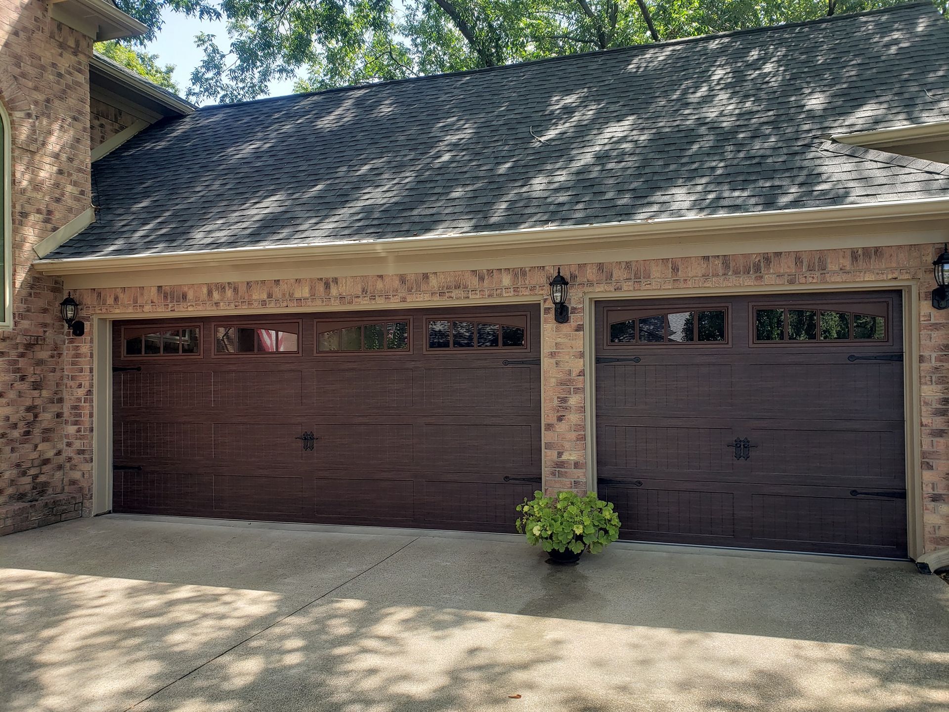 A brick house with two brown garage doors and a black roof.