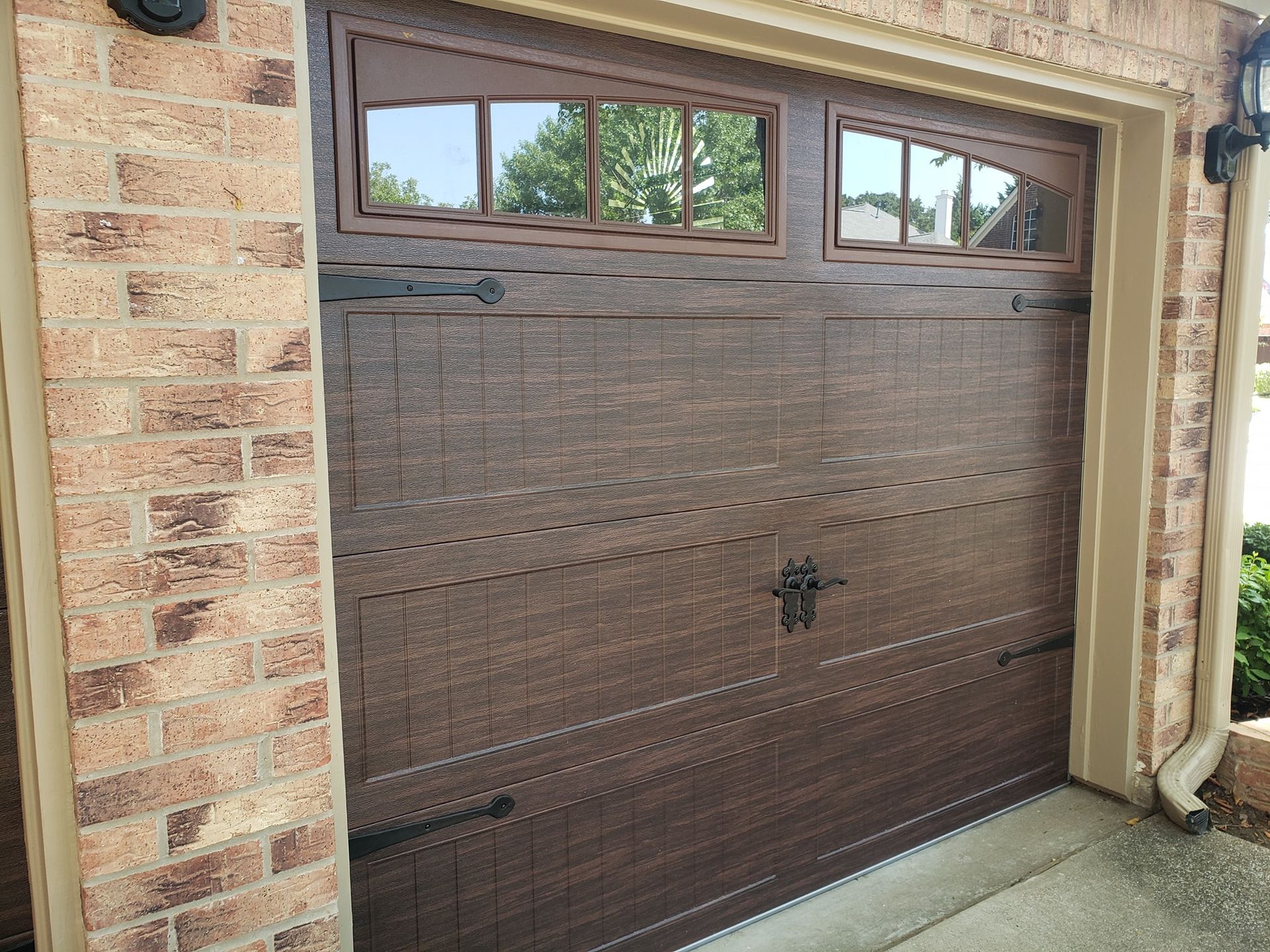 A brown garage door with a window on the side of a brick building.