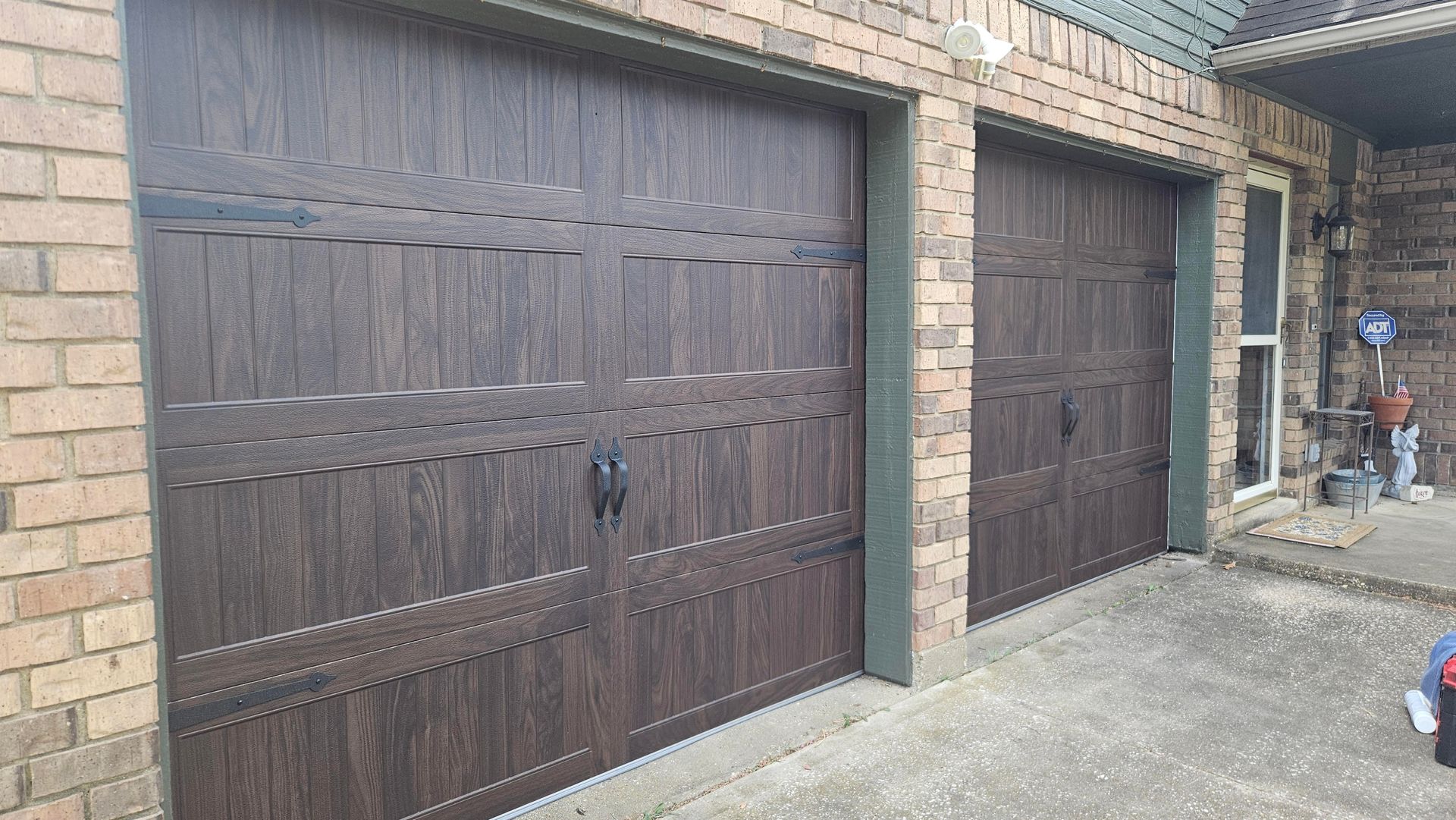 Two dark wood-look garage doors with black handles, set in a brick building exterior.