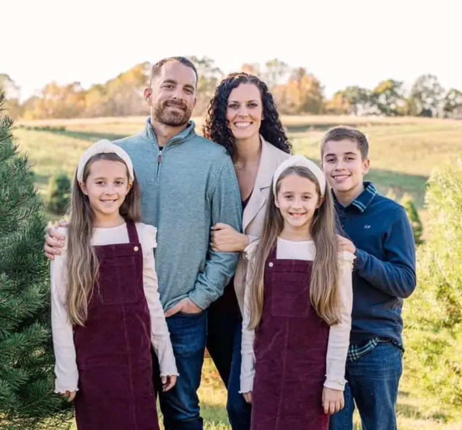 Family of five standing together in a grassy field, smiling at sunset.