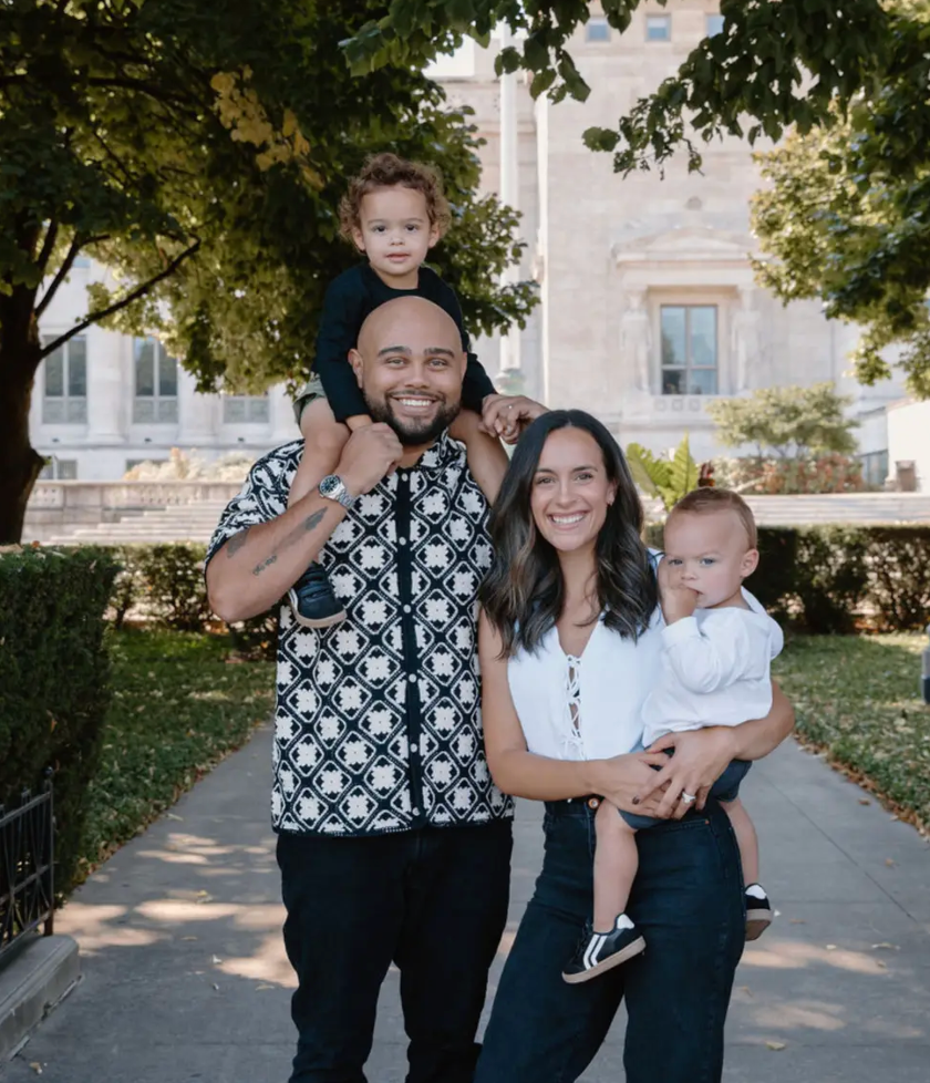 Family of four posing outdoors on a walkway, with two children and two adults in front of a building.