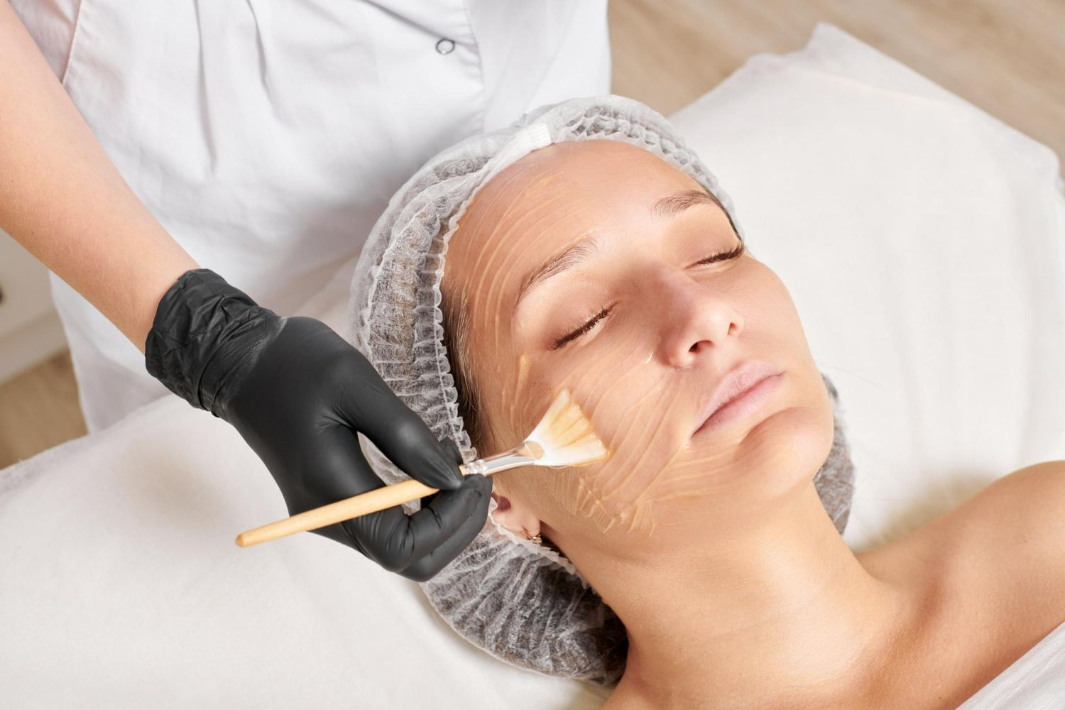 Person receiving facial treatment, being masked by gloved hand with brush.