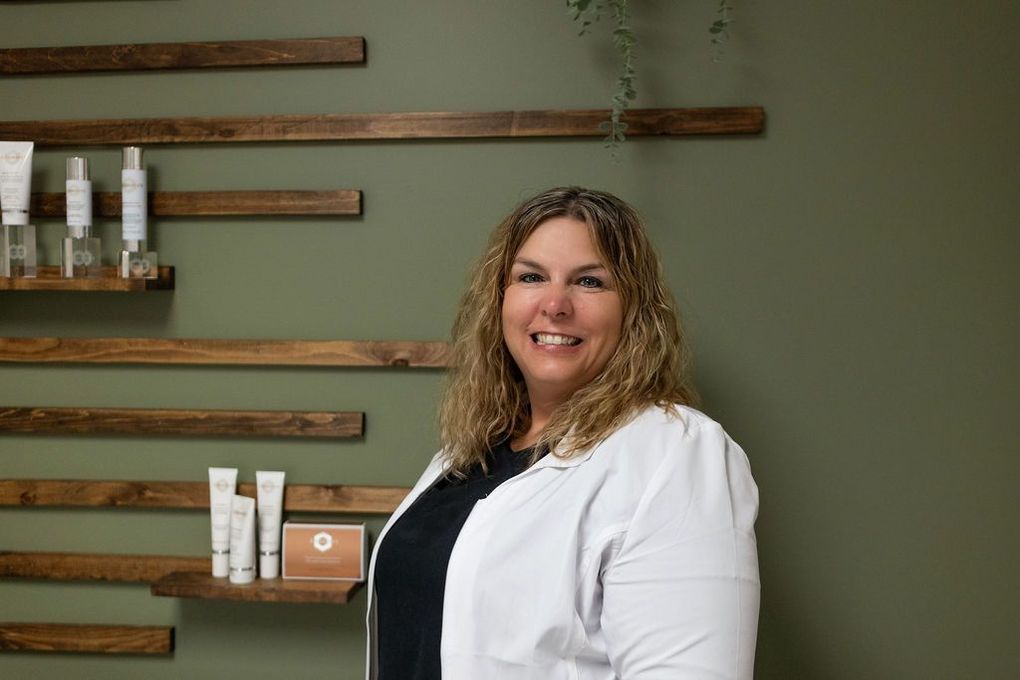 A woman in a white coat is standing in front of a shelf with cosmetics on it.