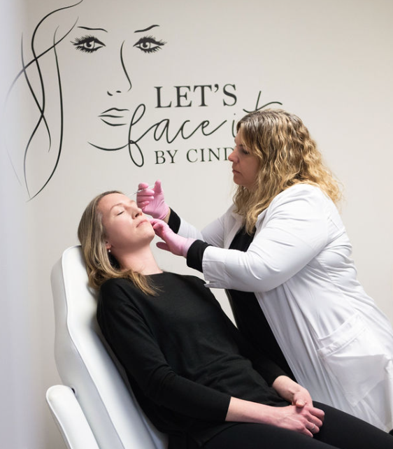 A woman is getting a botox treatment in front of a wall that says let 's face by cine