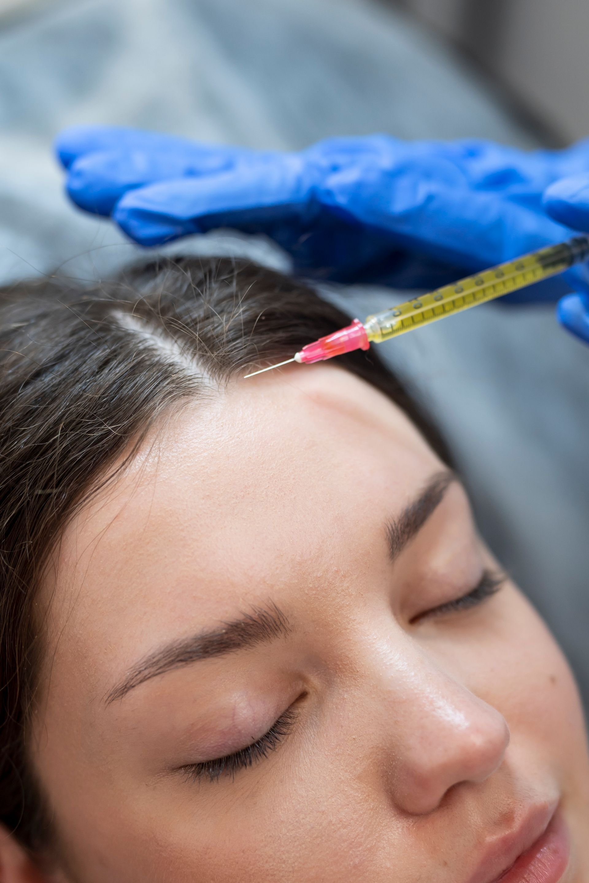A woman is getting a botox injection in her forehead.