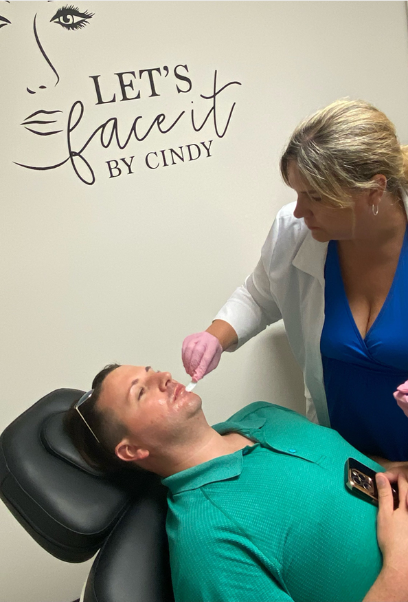 Woman administering facial treatment to a man in a medical setting.