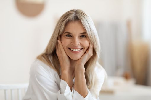 A woman with blonde hair is smiling with her eyes closed.