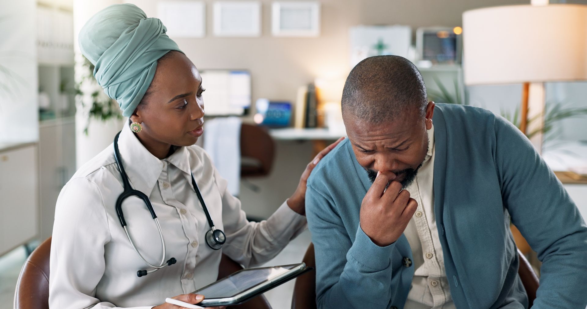A doctor is comforting a man who is crying while sitting in a chair.