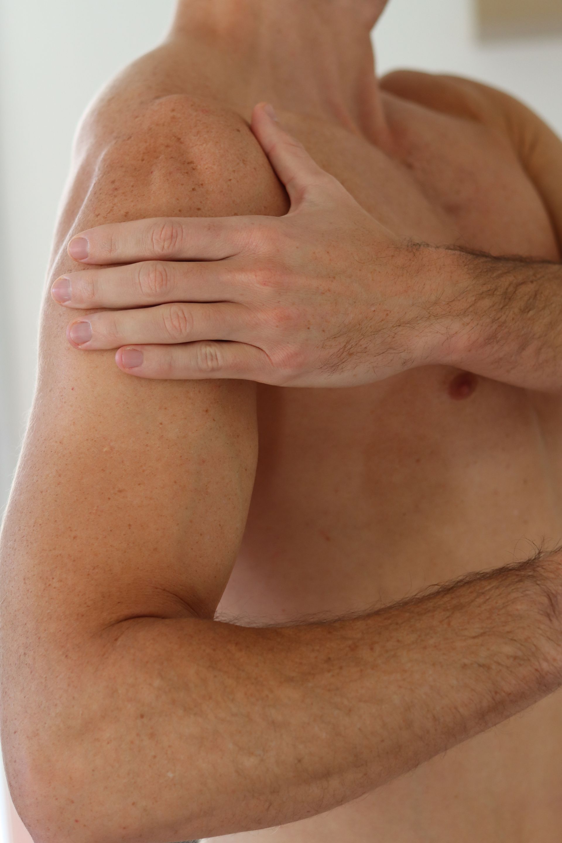 A shirtless man is holding his shoulder in pain.