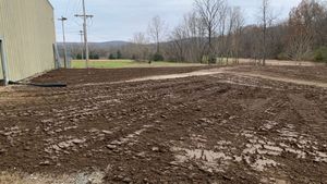 A muddy field with a building in the background and trees in the background.