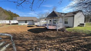 A white house with a porch is sitting in the middle of a dirt field.