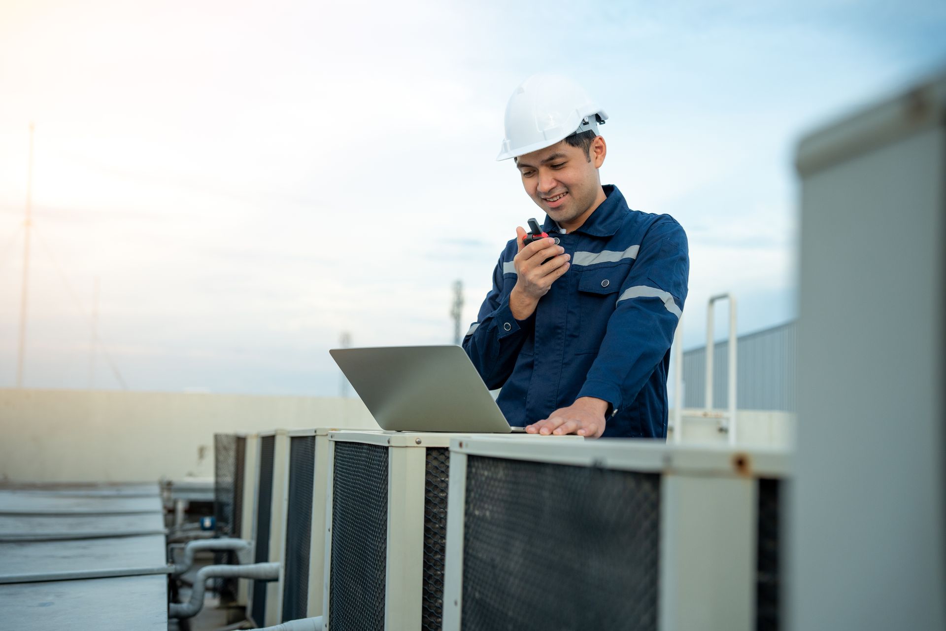 A man is talking on a walkie talkie while using a laptop computer.