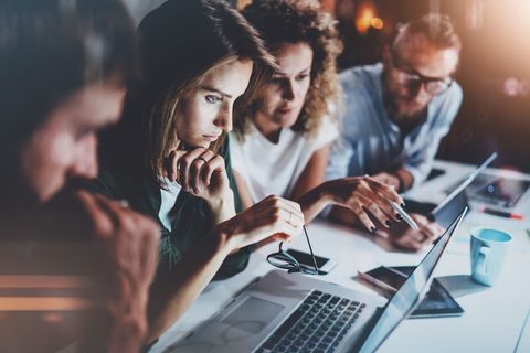 A group of people are sitting at a table looking at laptops.