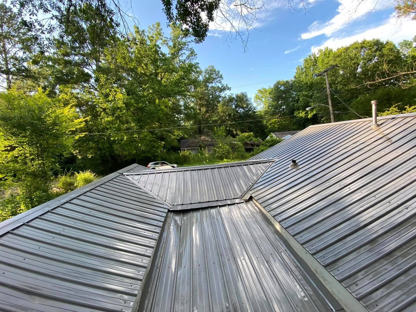 The roof of a house with a metal roof and trees in the background.