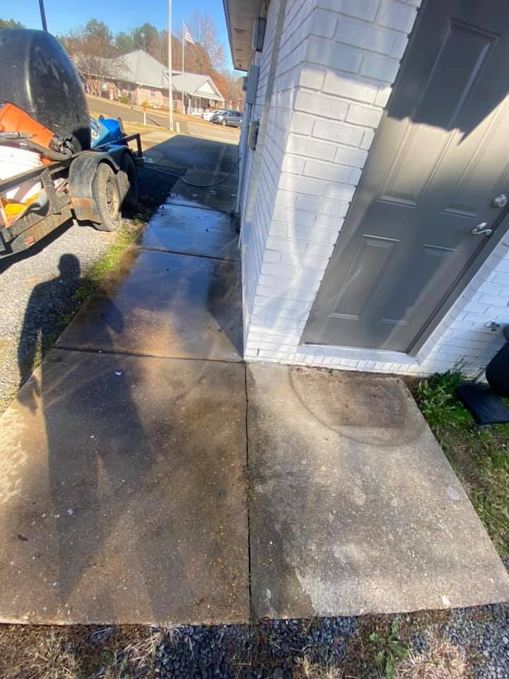 A concrete walkway next to a white brick building with a black door.