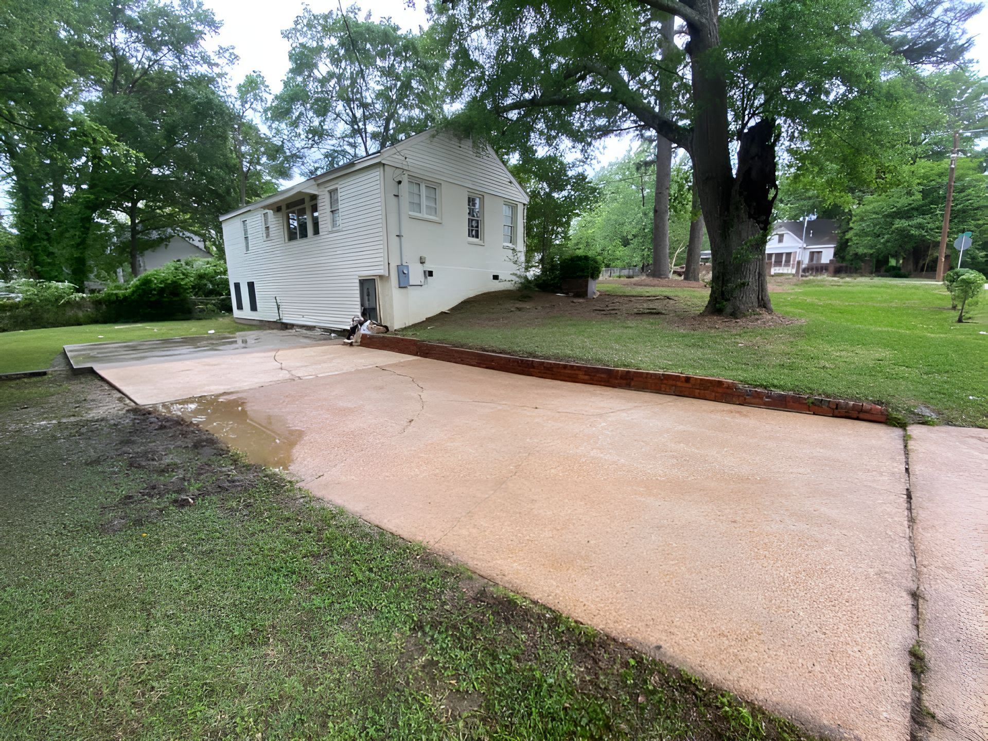 A white house is sitting on top of a grassy hill next to a concrete driveway.