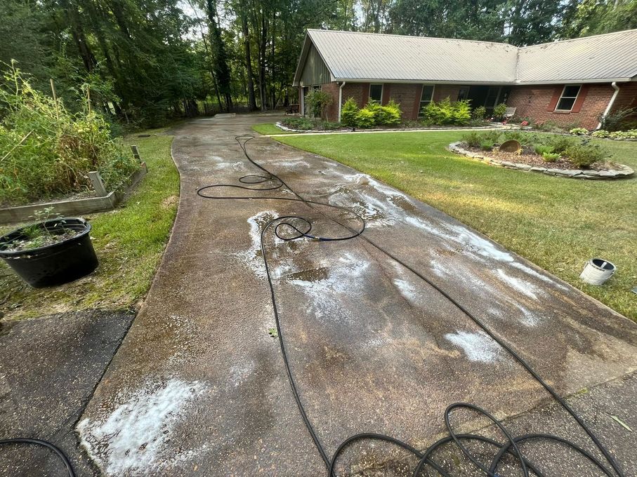 A driveway is being cleaned with a pressure washer in front of a house.