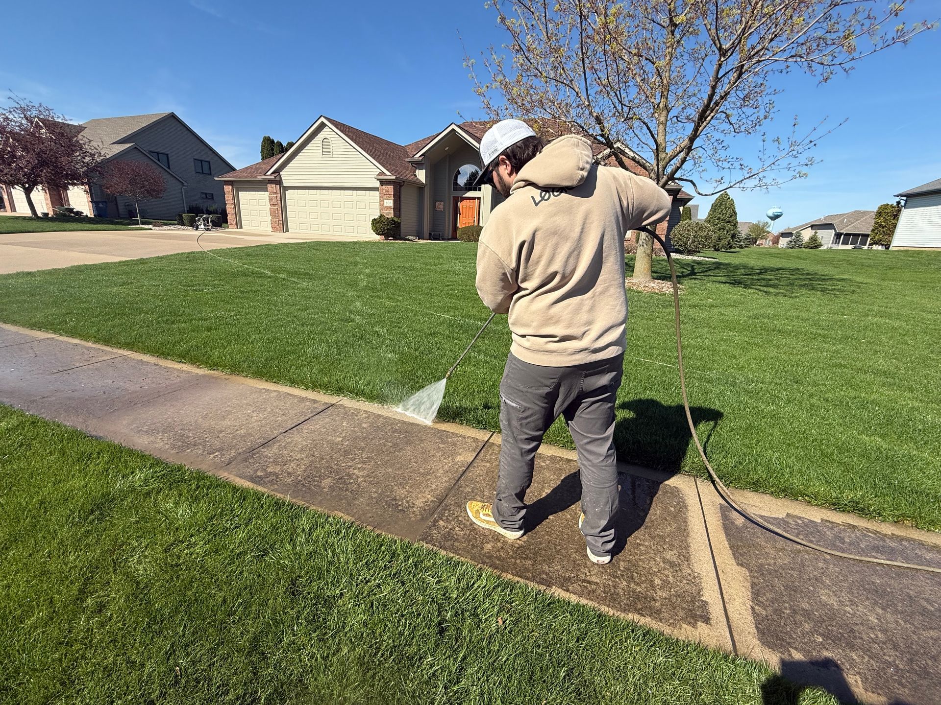 A man is using a high pressure washer to clean a sidewalk.